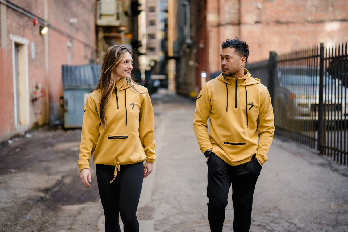 Man and woman walking in a Detroit alley wearing gold Riseabove Genesis Hoodies